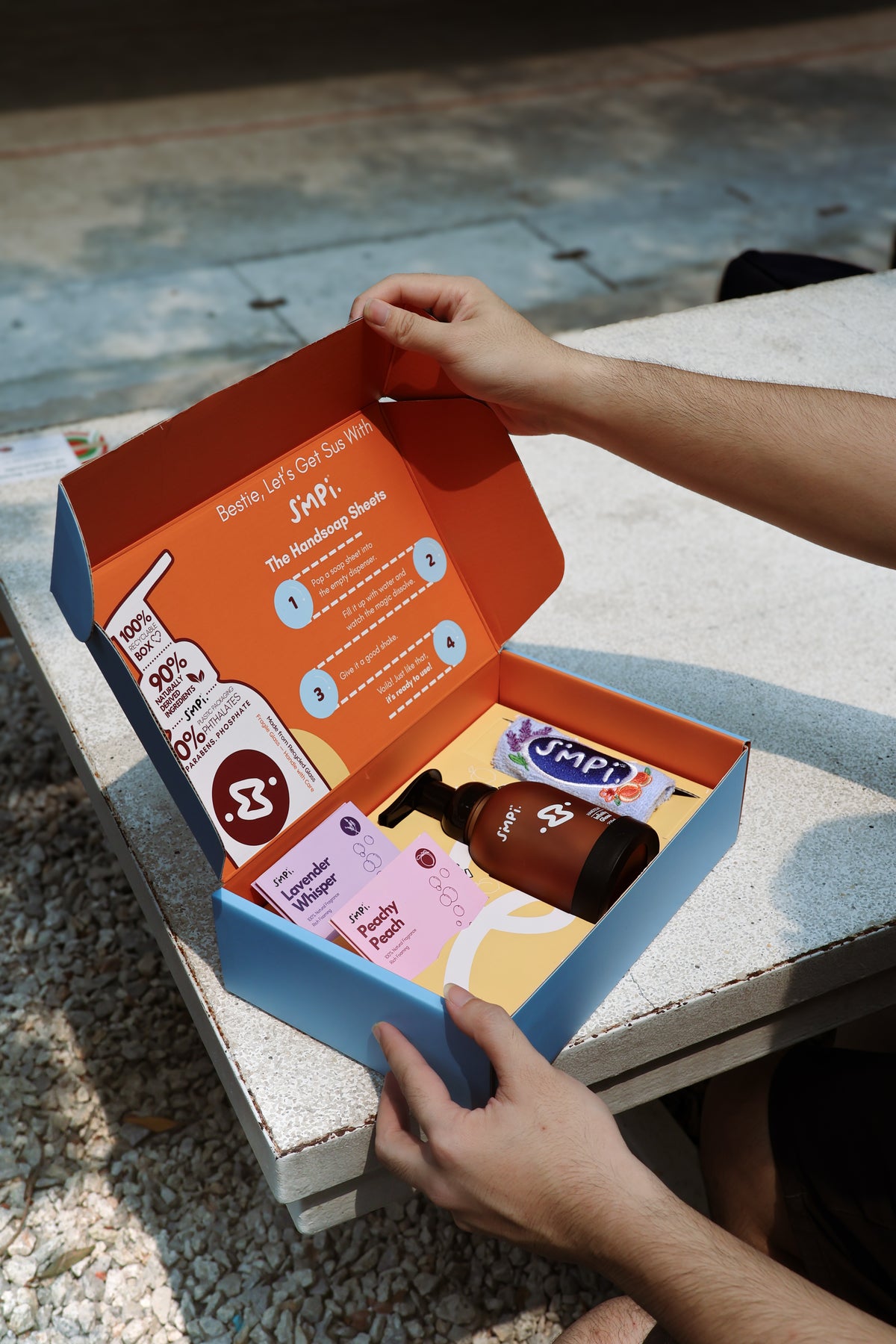 An open Simpi gift box with a glass foam dispenser, hand soap sheets and a towel